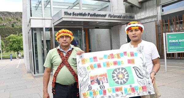 Two indigenous leaders holding up a banner outside of Scottish Parliament