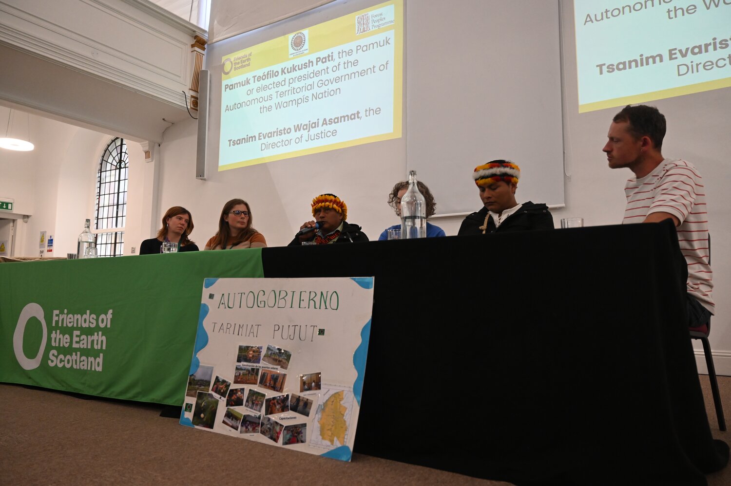 Six people sat at a table with a banner in front of them which reads 'friends of the earth'