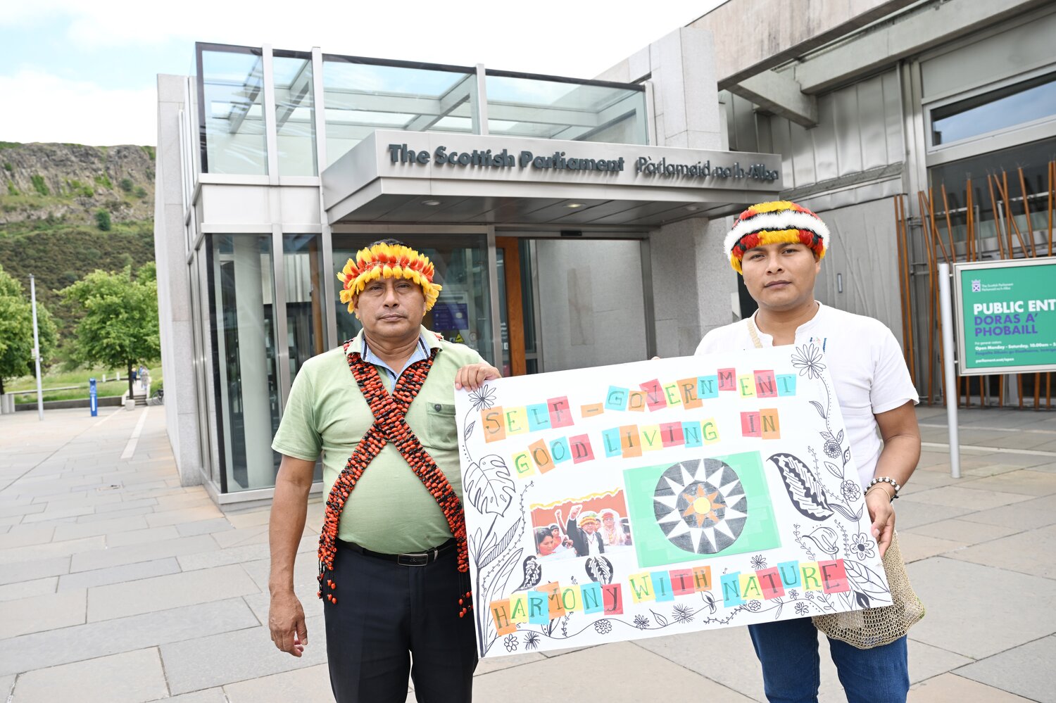 Two people holding a sign stood outside the Scottish parliament entrance