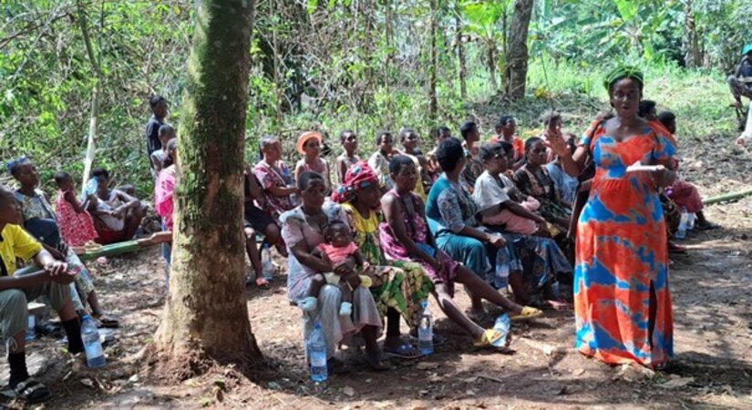A person in orange talks to people sat in a forest