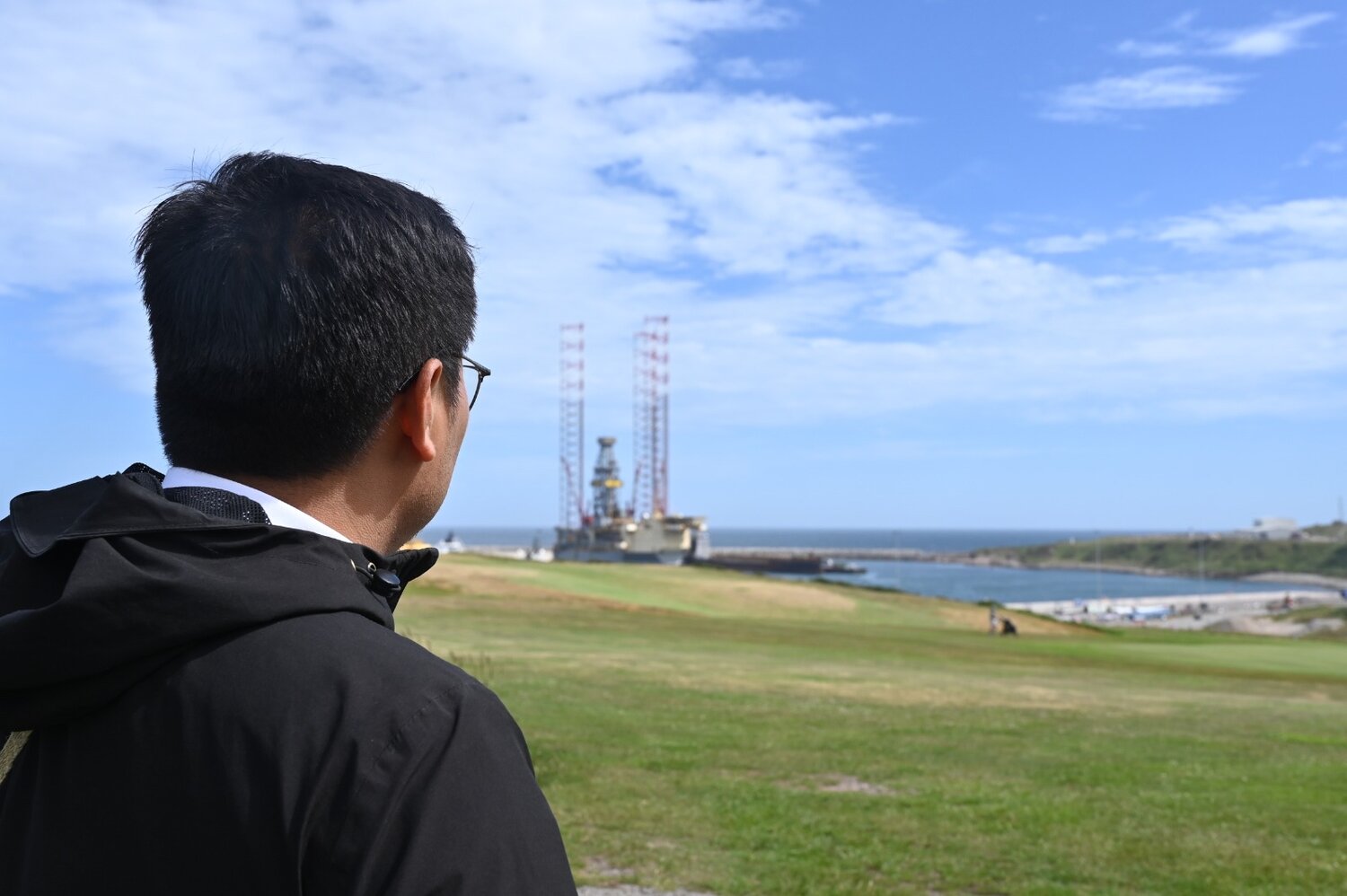 A man looking onto a bay with an oil rig.