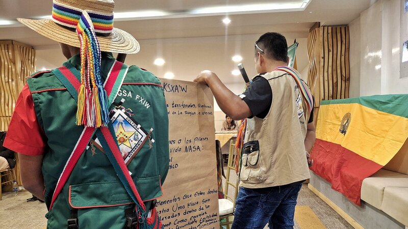 Photo shows the backs of two Colombia territorial defenders holding a sheet of paper with writing on it. The defenders were gathering in Bogotá to exchange strategies on access to justice and challenging harmful mineral and hydrocarbon activities.