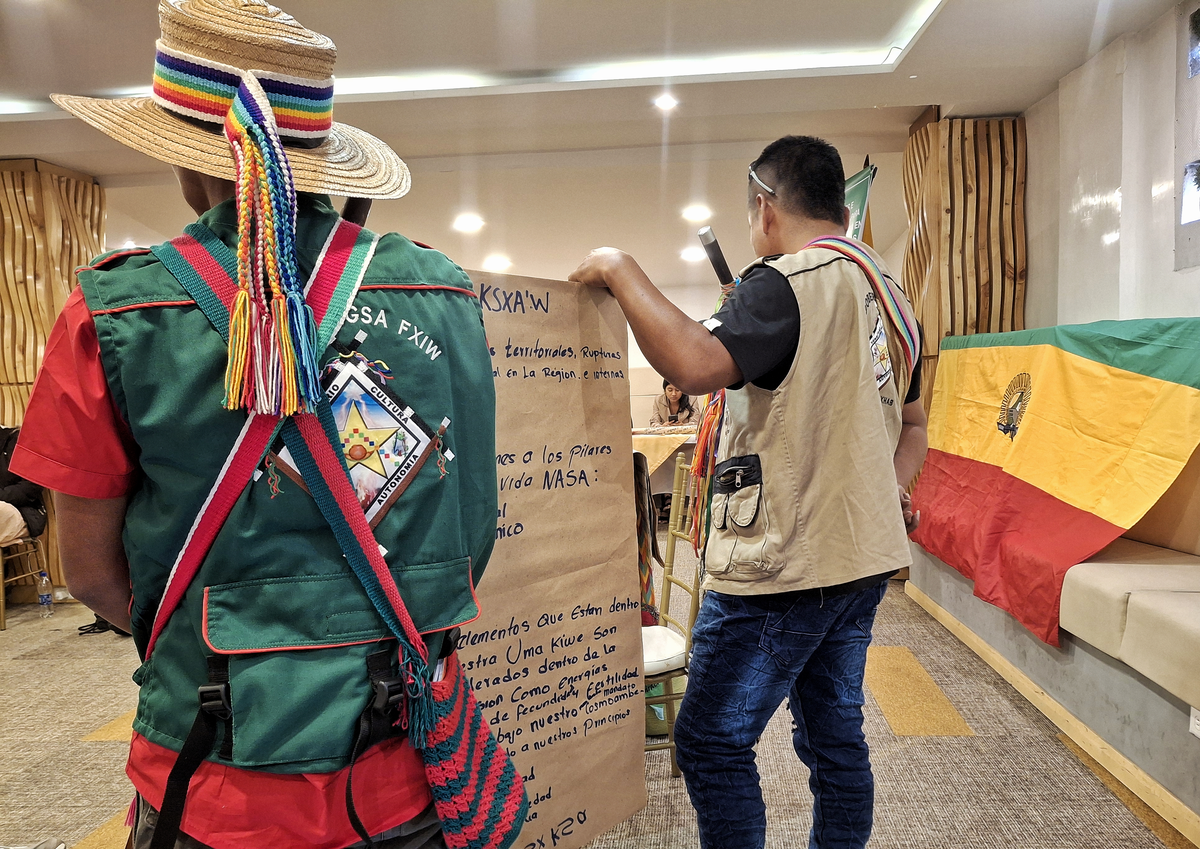 Photo shows the backs of two Colombia territorial defenders holding a sheet of paper with writing on it. The defenders were gathering in Bogotá to exchange strategies on access to justice and challenging harmful mineral and hydrocarbon activities.